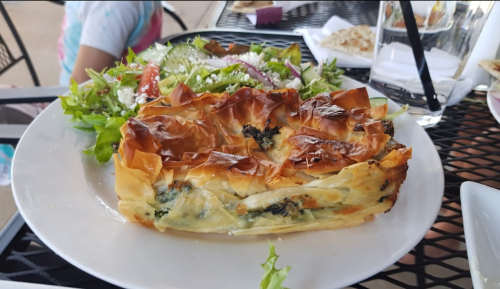 A plate with a slice of flaky pastry filled with greens, alongside a fresh salad with mixed vegetables.